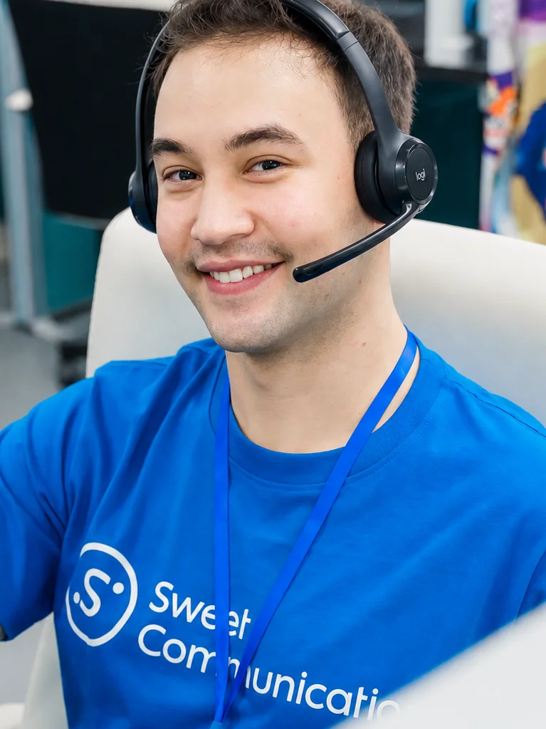 Leende medarbetare med headset i Sweet Communication-tröja vid sitt skrivbord